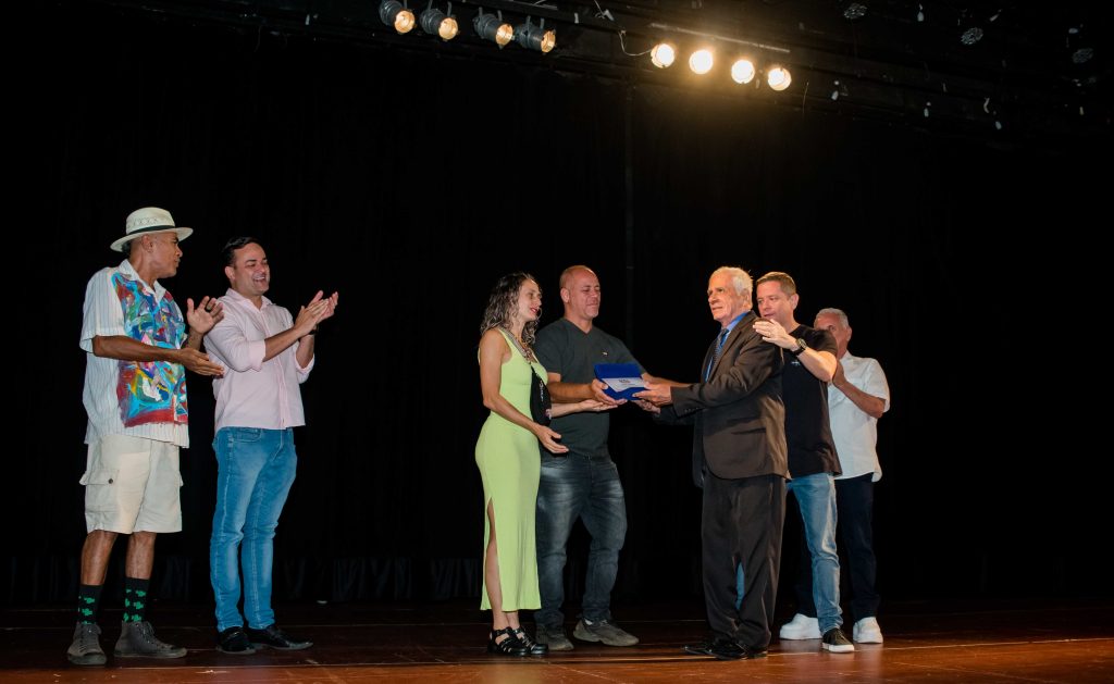 (27.03.2023) — Paulo Sanches recebe a placa de homenagem da Semana Boca de Cena das mãos de Márcio Veiga e Trásrila Bonelli. Foto: @teroqueiroz | @teatrinetv