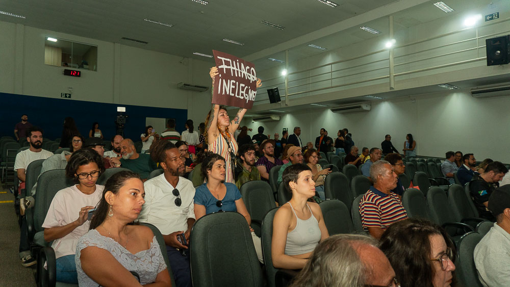 (14.dez.23) - A artista visual Thaly Veron ergue cartaz lembrando a situação de inegibilidade de Tiago Vargas, condenado e que portanto não pode concorrer no próximo ano. Foto: Tero Queiroz