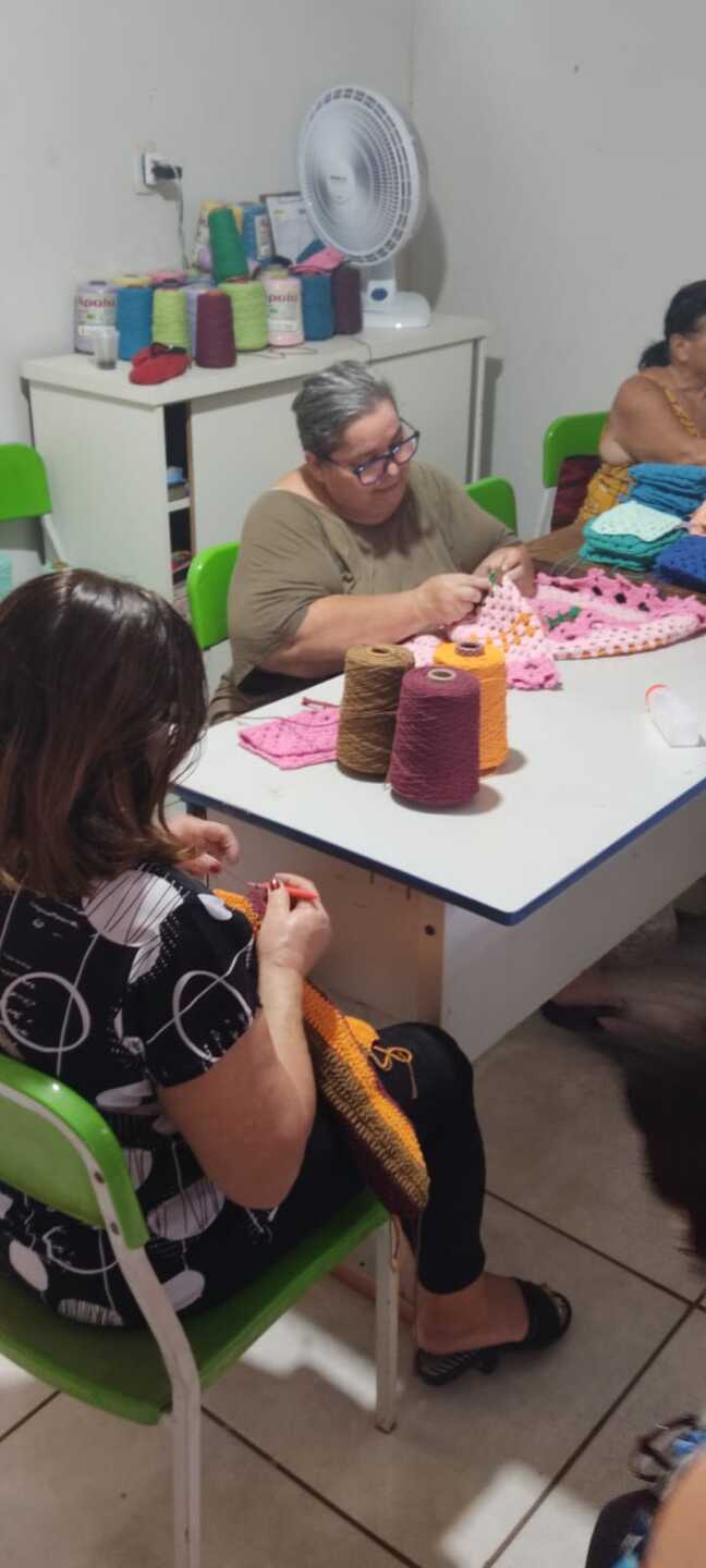 Elita Rodrigues de Andrade Medeiros, de óculos e blusa bege, trabalha em uma peça de crochê em tom rosa claro. Foto: Reprodução